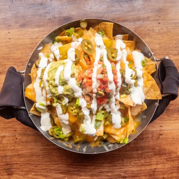 A skillet of nachos with melted cheese, guacamole, pico de gallo, sour cream, and jalapeños.