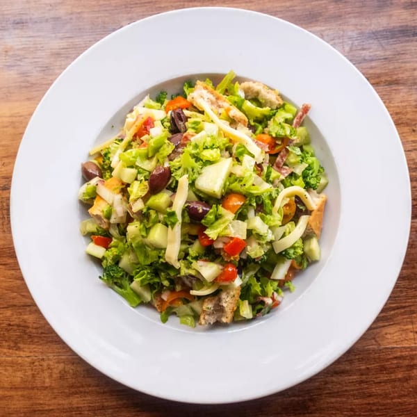 A vibrant salad with lettuce, tomatoes, olives, and croutons in a white bowl on a wooden table.