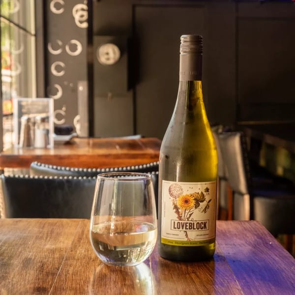 A bottle of Loveblock Sauvignon Blanc and a glass of white wine on a wooden table.