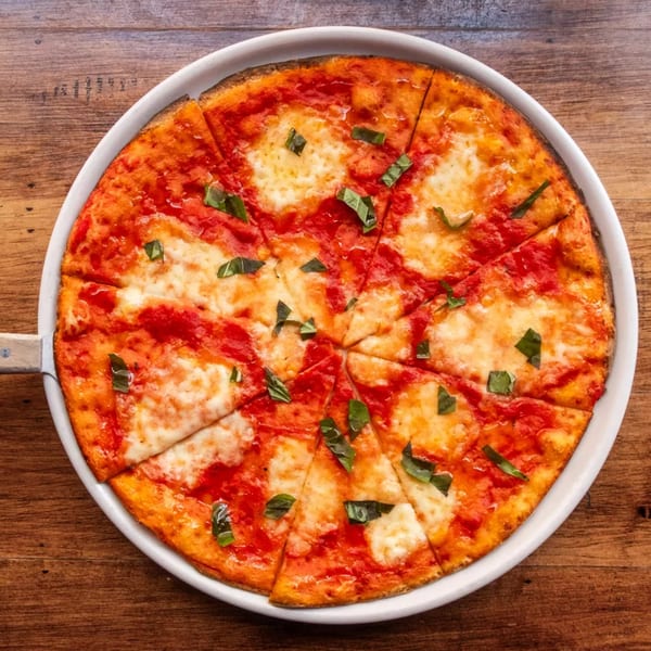 A sliced Margherita pizza with red sauce, melted mozzarella, and fresh basil on a white plate.