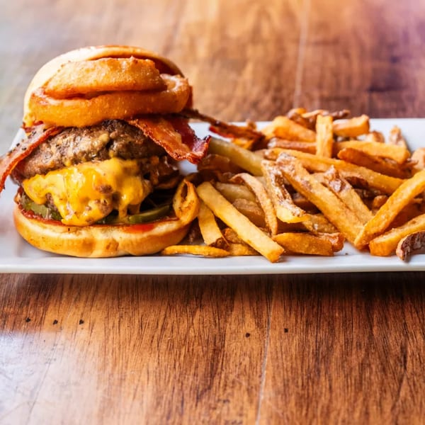 A bacon cheeseburger with onion rings and a side of french fries on a white plate.
