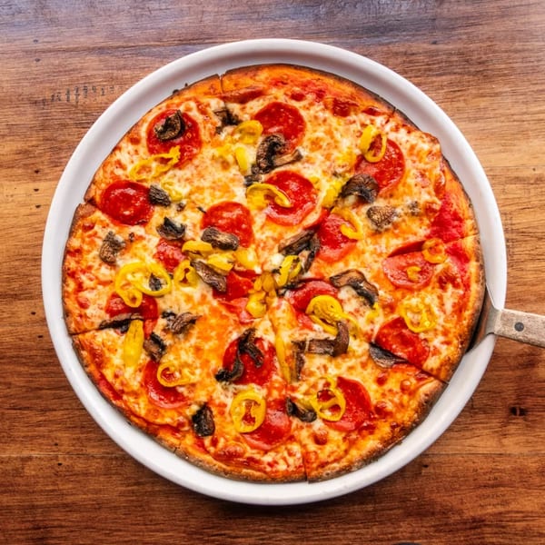 A whole pepperoni, mushroom, and banana pepper pizza on a white plate with a server.
